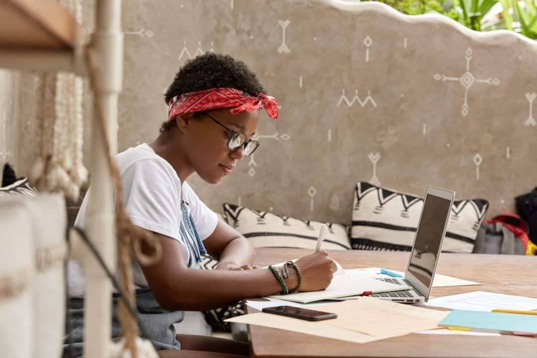 A young woman writing on a laptop at a table.
